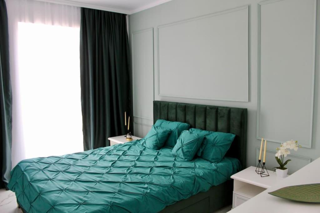 a bed with a green comforter in a bedroom at Luxe Central Apt: Free Parking in Oradea