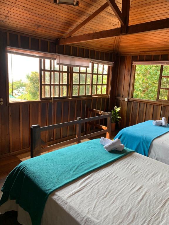 two beds in a room with wooden walls and windows at Morada Sunset Praia do Rosa in Praia do Rosa
