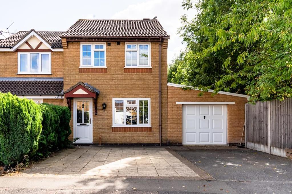 een bruin bakstenen huis met witte garagedeuren bij Cheerful 3 Bedroom Family Home with parking in Leicester