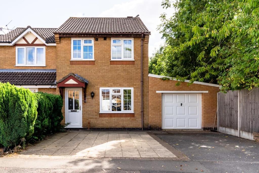 a brown brick house with white garage doors at Cheerful 3 Bedroom Family Home with parking in Leicester