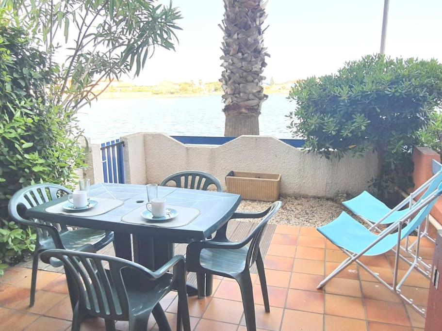 - une table et des chaises sur une terrasse à côté de l'eau dans l'établissement Charmant T1 Barcarès Soleil Bleu, au Barcarès