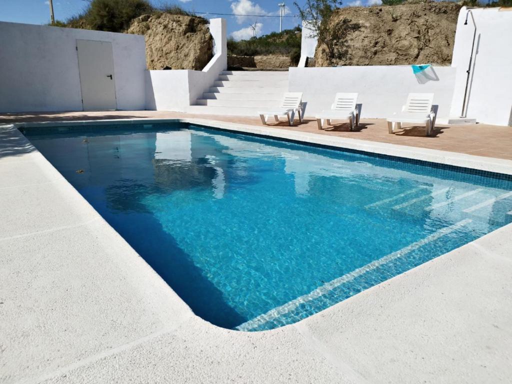 a swimming pool with chairs and blue water at Molino Viejo, Jauca Baja, 04899 El Hijate, Almeria Province Spain in El Hijate