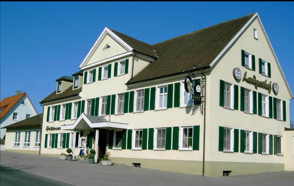 ein großes weißes Gebäude mit grünen Rollläden auf einer Straße in der Unterkunft Gasthof Goldenes Lamm in Schwabsberg