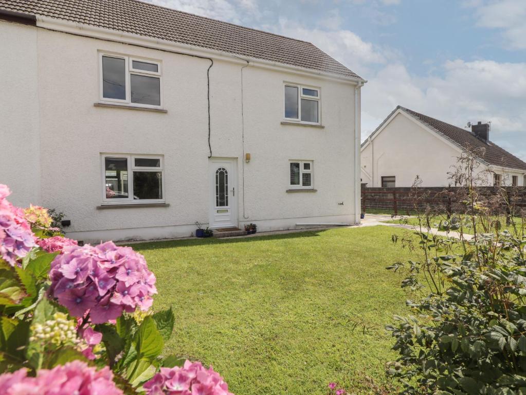 a white house with pink flowers in the yard at Ty Beca in Clynderwen