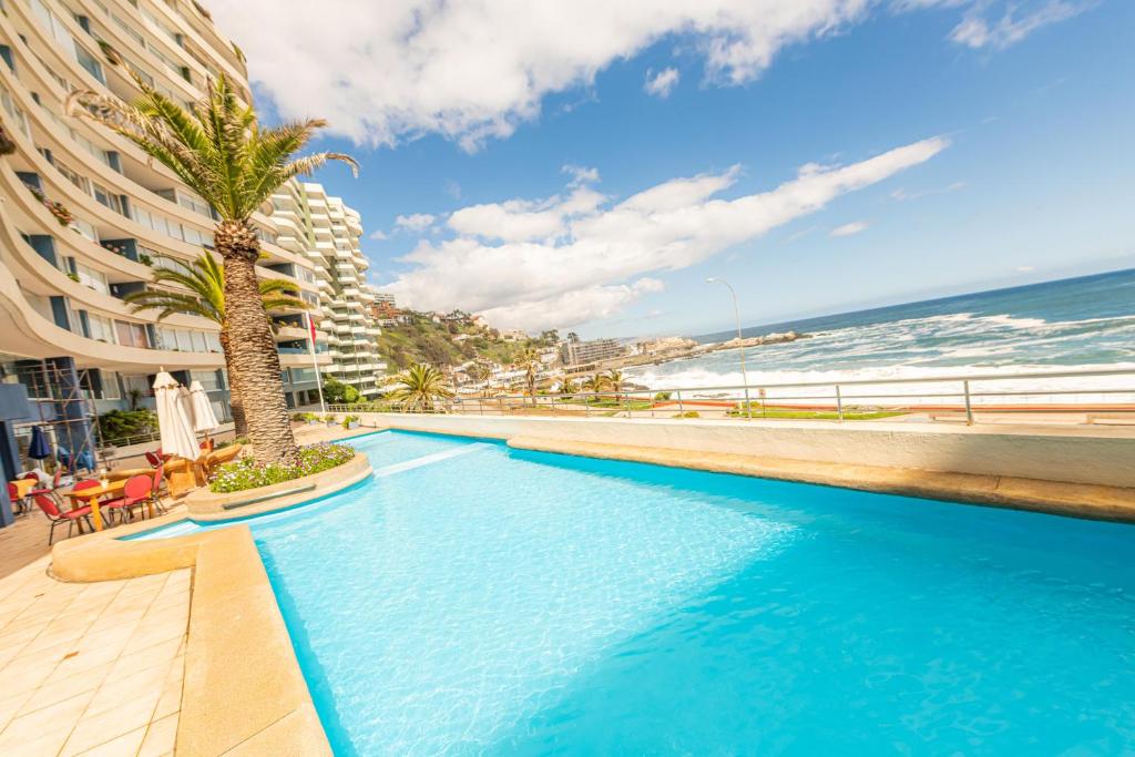 a swimming pool next to a beach and a building at Oceana Suites Eurovista in Viña del Mar