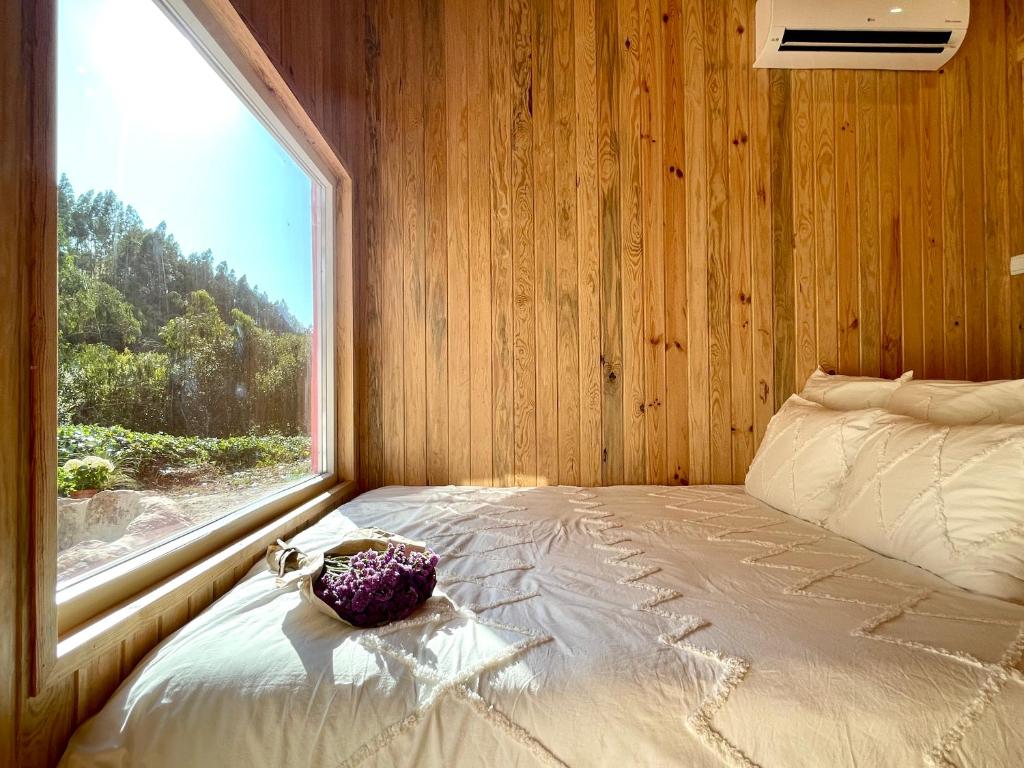 a bedroom with a bed with a large window at Nativo Natureza Pink Wood Cabin in Cela