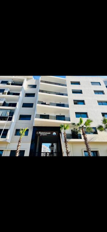 een hoog wit gebouw met palmbomen ervoor bij Luxurious Mannesmann Beach in Mohammedia