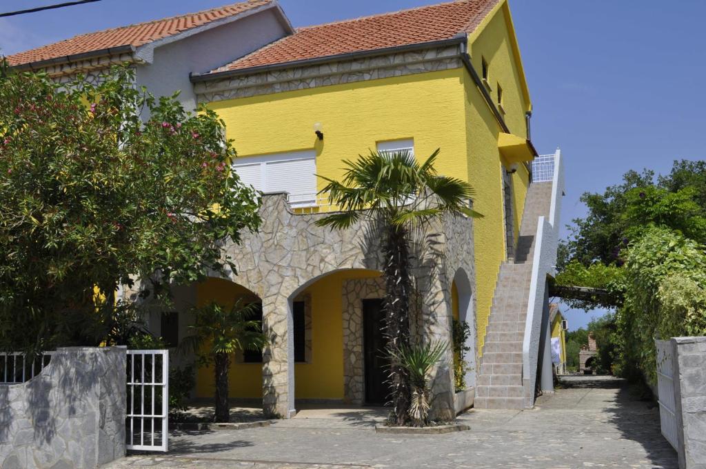 una casa amarilla con una palmera delante de ella en Apartments Pavlović en Linardići