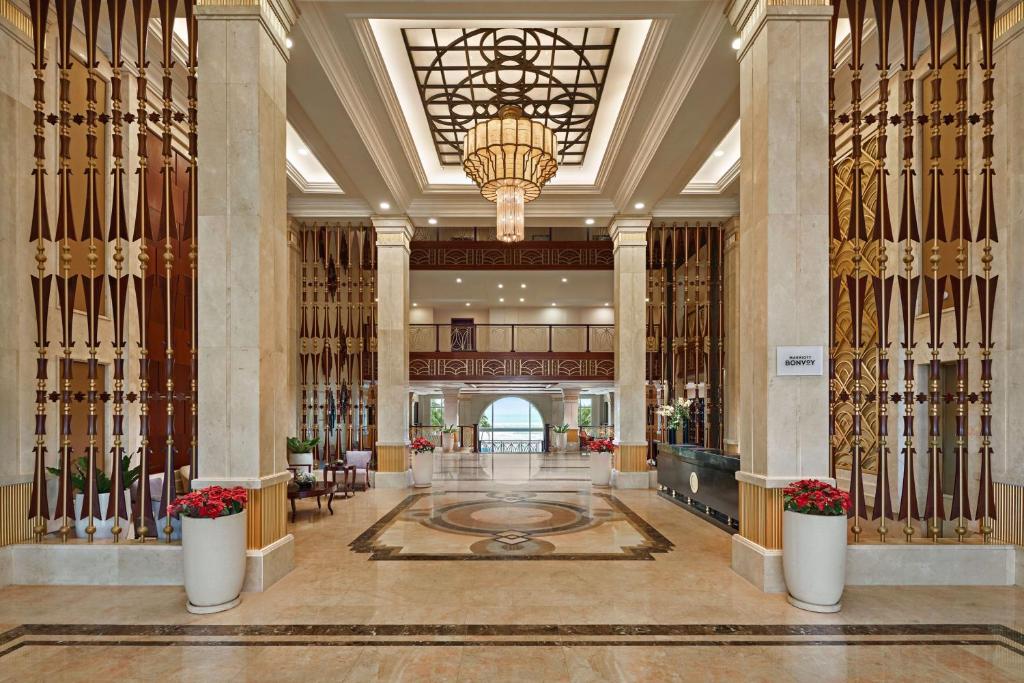 A grand marble lobby opens toward a bright arched view, beneath a large chandelier.