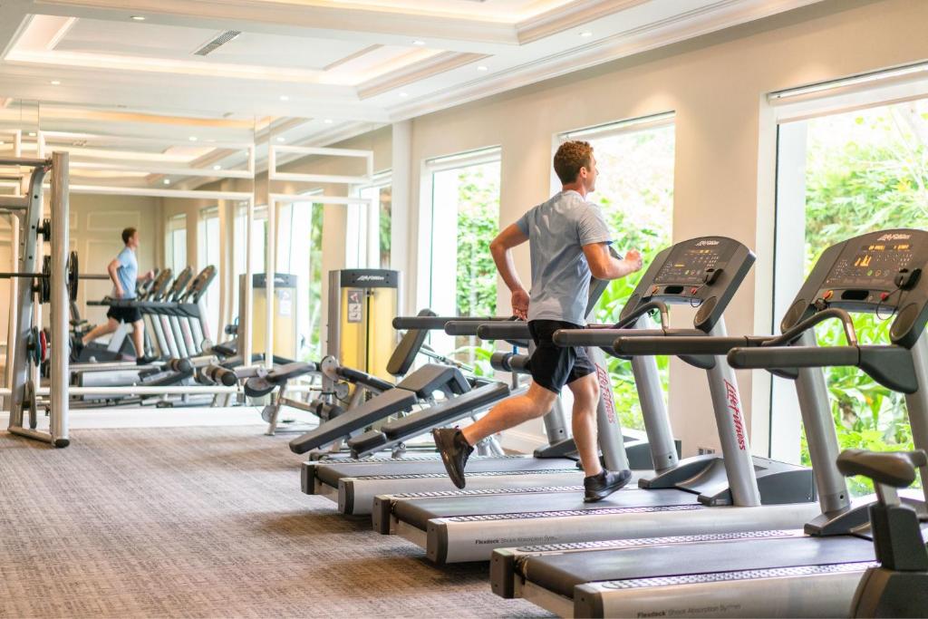 A guest runs on a treadmill in a windowed fitness room with additional cardio and strength equipment.