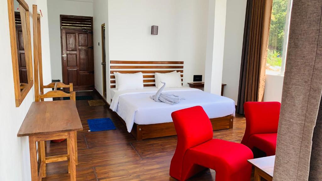 a bedroom with a bed and two red chairs at Nilowin Glenanore Guesthouse in Haputale