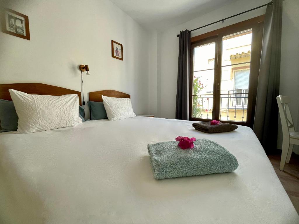a bedroom with a white bed with a towel and a window at Boutique Hostal Lorca in Nerja