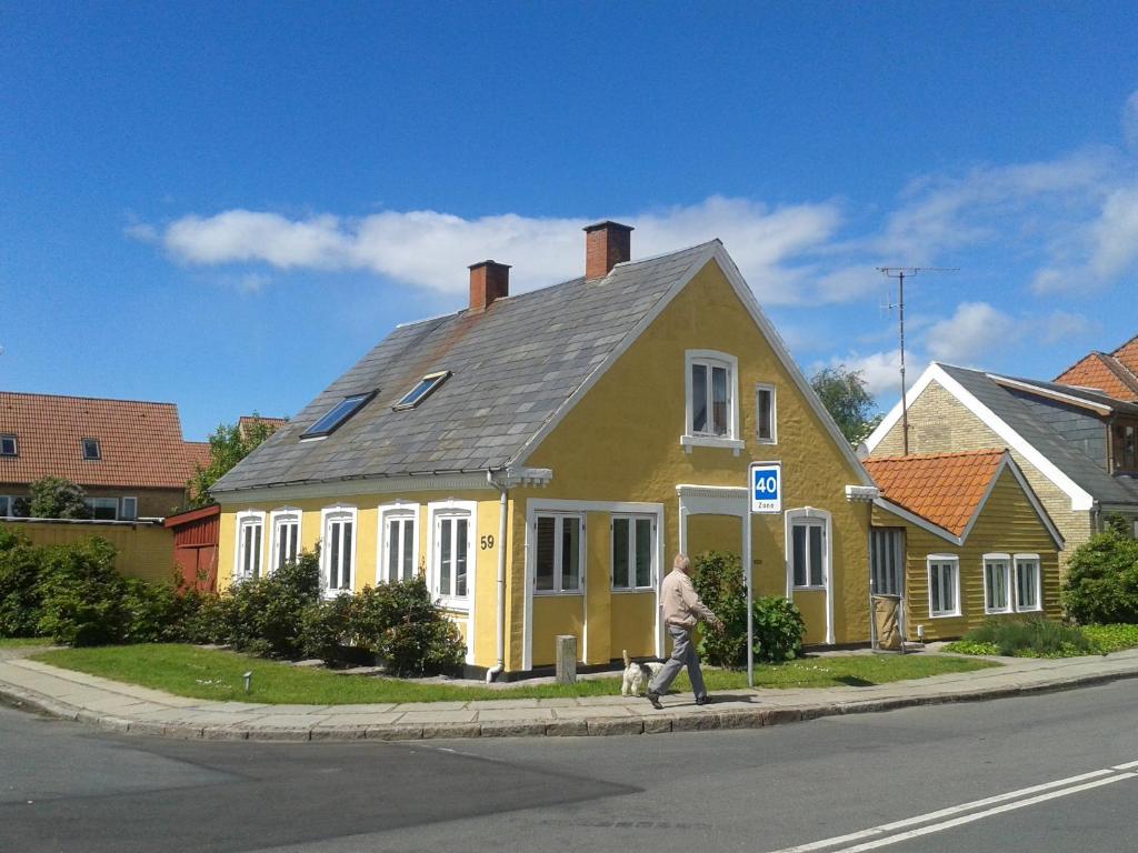 un homme marchant un chien devant une maison jaune dans l'établissement Belvedere B&B, à Svendborg