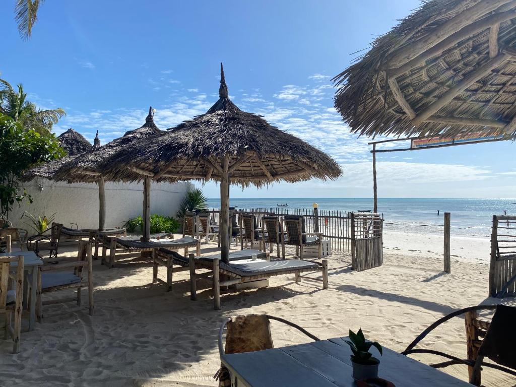 una playa con mesas y sombrillas de paja y el océano en Bahari Beach Bungalows, en Jambiani