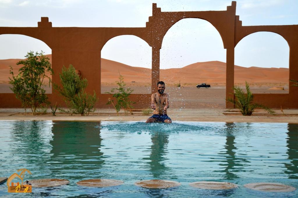 un hombre sentado en un charco de agua en el desierto en Kasbah Du Berger & Piscine en Merzouga