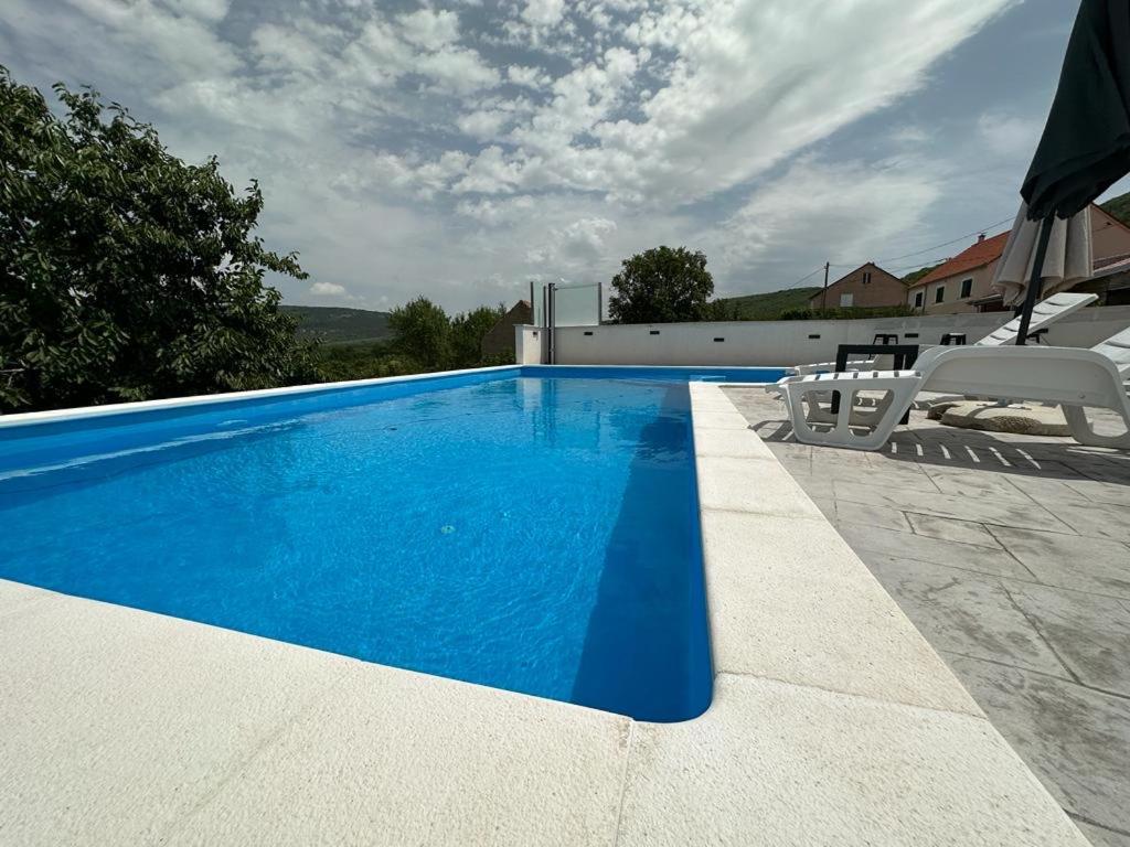 een blauw zwembad met twee witte stoelen ernaast bij Villa Green Hill, Cista Velika, Omis hinterland in Omiš