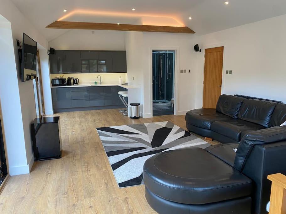 a living room with a black leather couch and a kitchen at Stansted Airport Luxury Annexe with Parking. in Birchanger