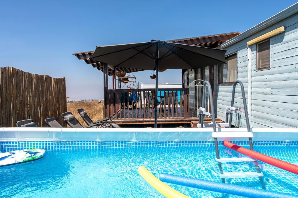 uma piscina com um guarda-sol ao lado de uma casa em הבקתה הכחולה - The blue cabin em Sha'al