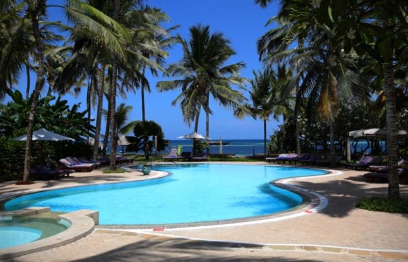 einen großen Pool mit Palmen und dem Meer in der Unterkunft Turtle Bay Beach Club in Watamu