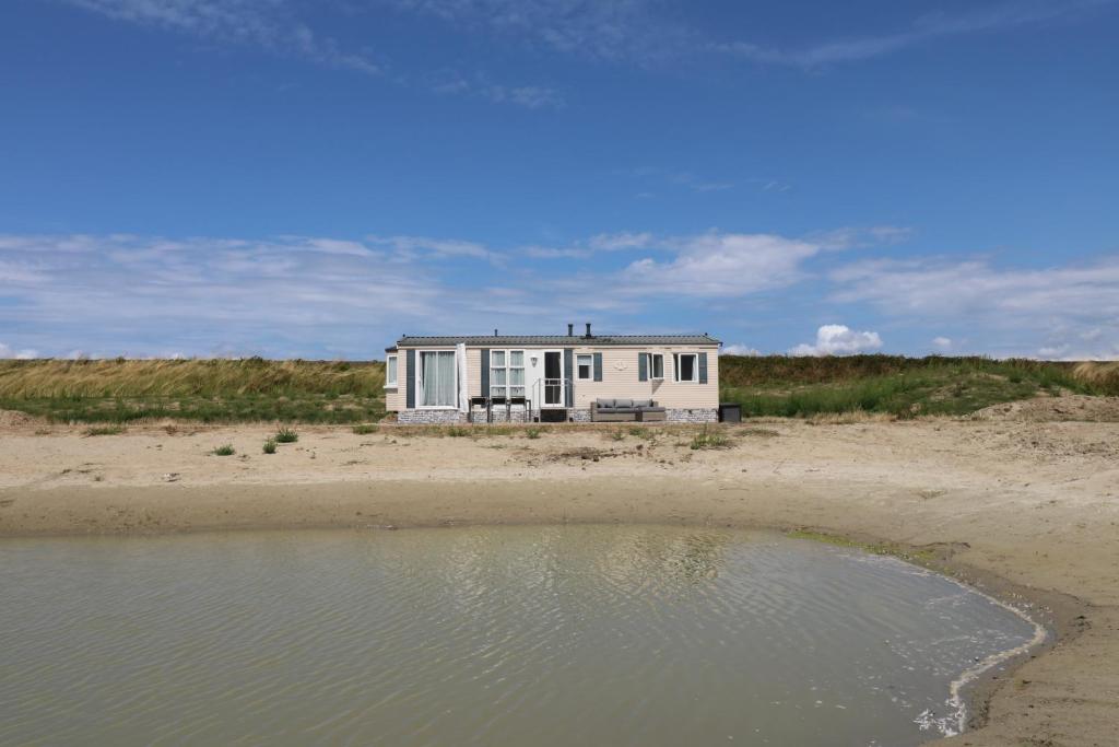 una casa blanca en la playa con un cuerpo de agua en De Zuidvliet Chalet 4, en Wolphaartsdijk