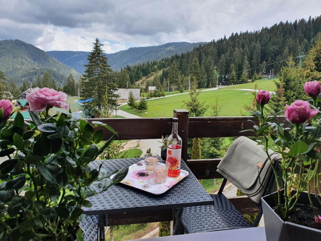 einen Tisch mit einem Getränk und Gläsern auf einem Balkon mit Rosen in der Unterkunft Vlašićka ruža Eko FIS 303 in Vlasic
