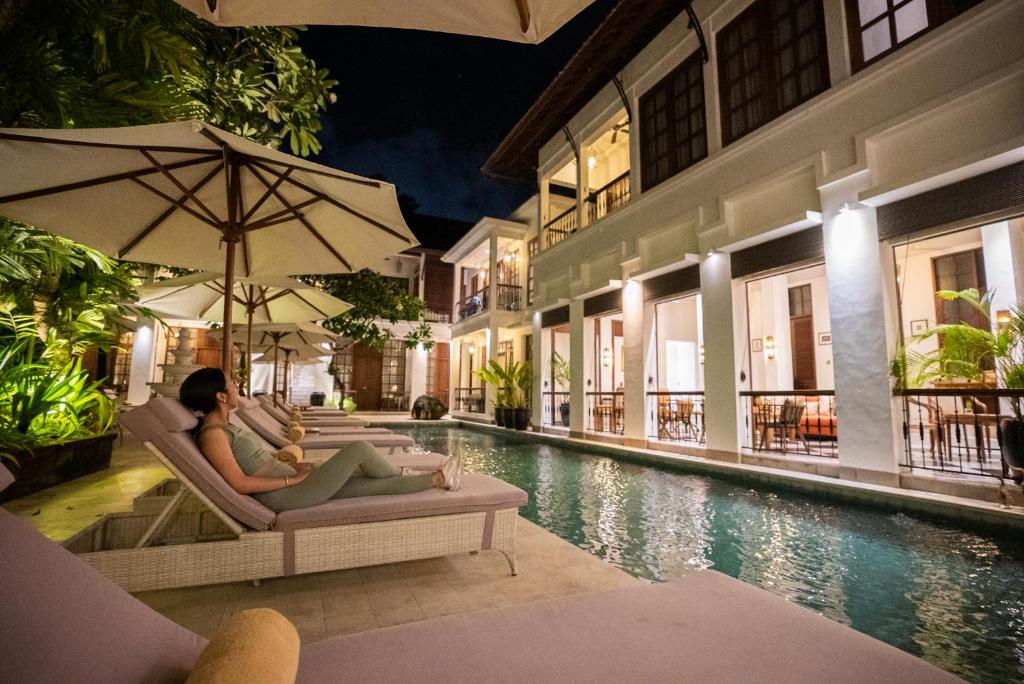 una coppia seduta su sedie accanto alla piscina di un hotel di The Colony Hotel Bali a Seminyak