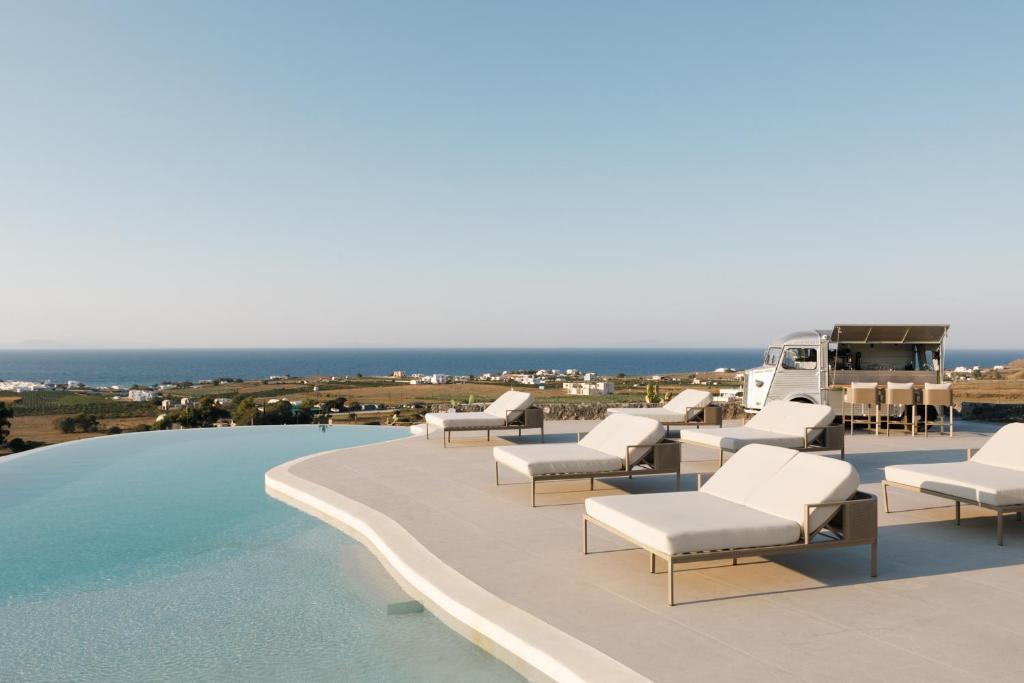 a pool with lounge chairs and the ocean in the background at Elysian Retreat in Oia