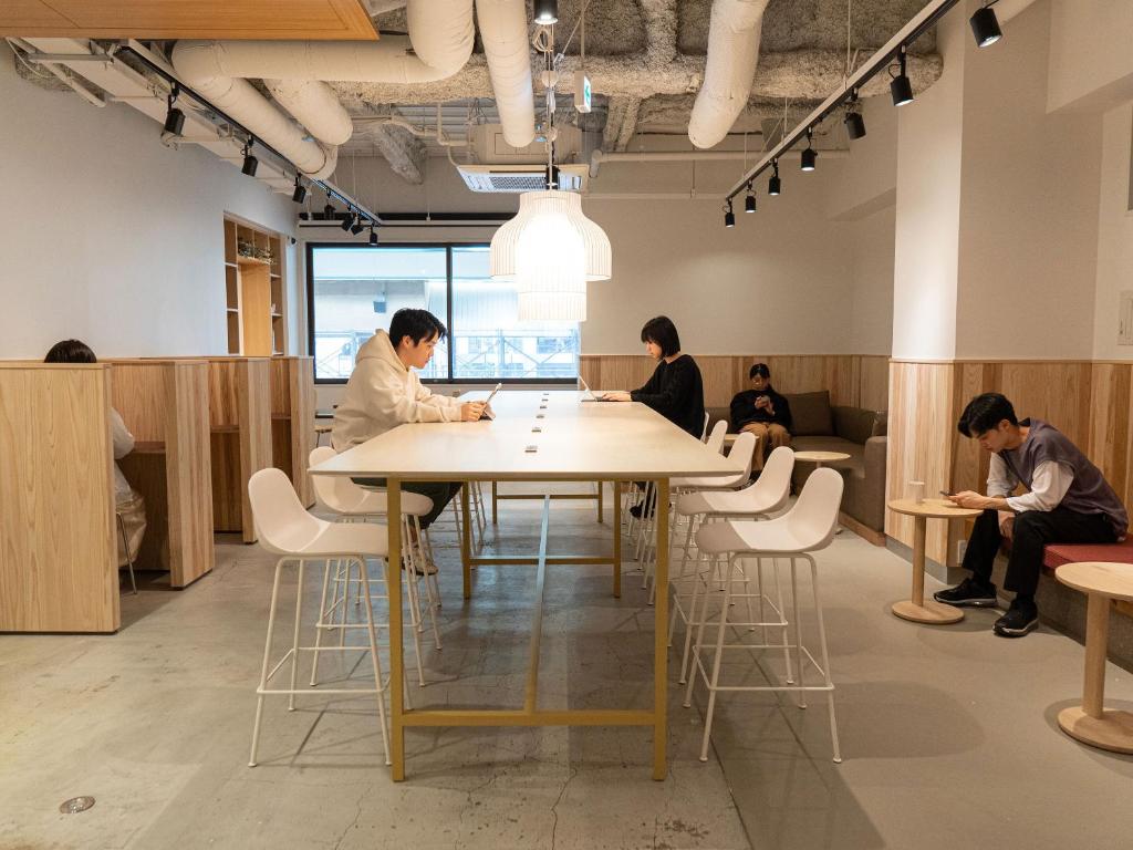 eine Gruppe von Menschen, die in einem Raum an einem Tisch sitzen in der Unterkunft Hotel Plus Hostel SAPPORO in Sapporo