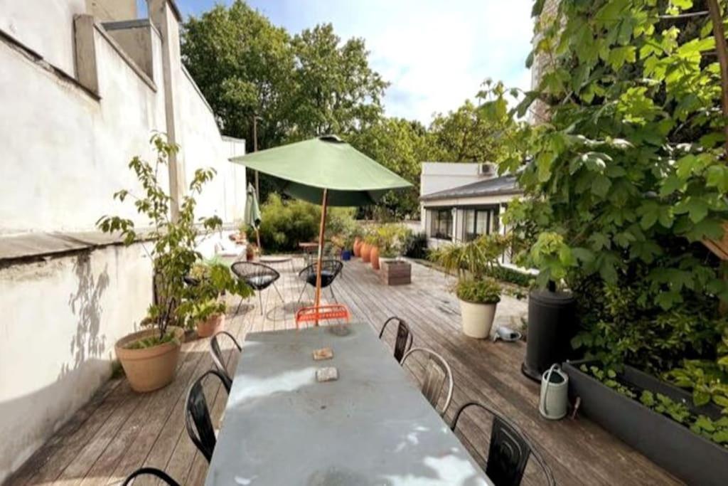 uma mesa e cadeiras num deque com um guarda-sol em Loft familial avec grand jardin verdoyant em Paris