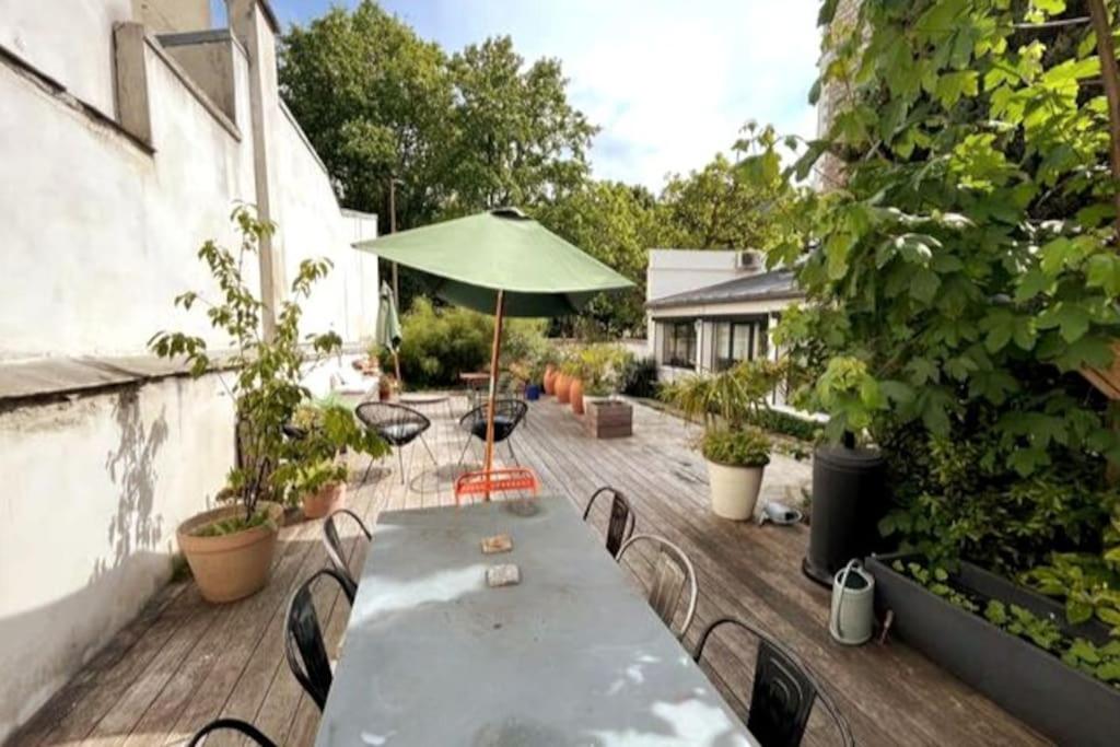 une table et des chaises sur une terrasse avec un parasol dans l'établissement Loft familial avec grand jardin verdoyant, à Paris