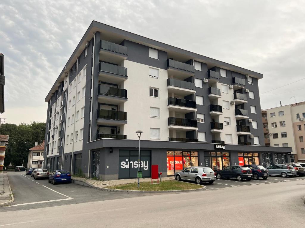 Un gran edificio con coches aparcados en un estacionamiento. en Apartman Max, en Modriča