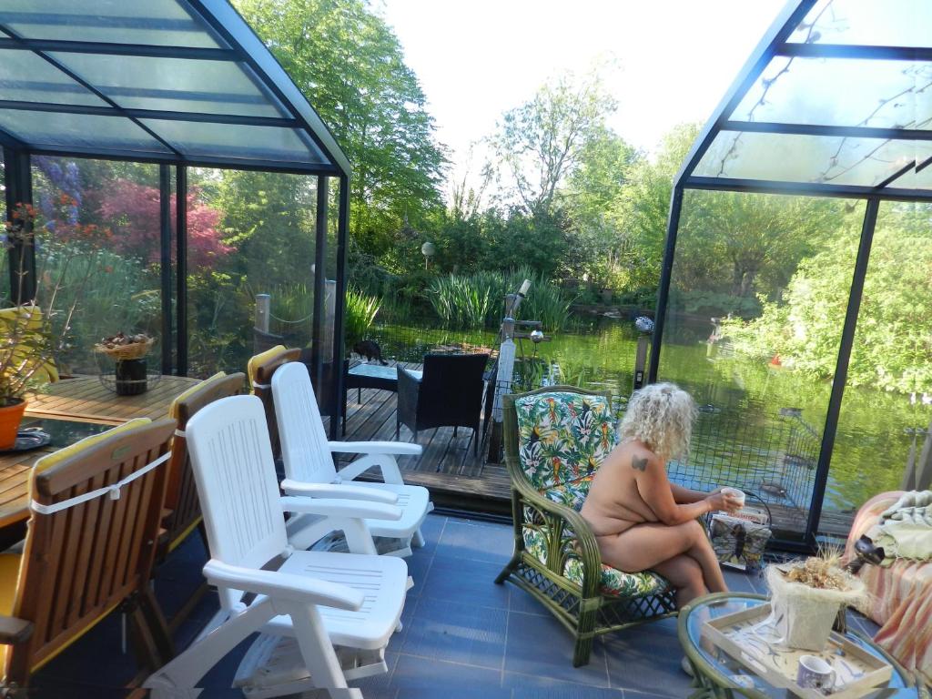 an older woman sitting on a screened porch with a view of a garden at chambres d'hôtes naturistes de la moque souris in Saint-Pierre-de-Mailloc