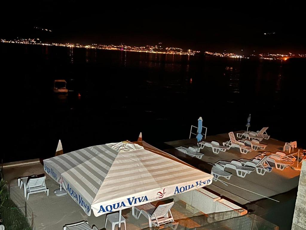 eine Terrasse mit einem Sonnenschirm und Stühlen am Wasser in der Nacht in der Unterkunft Zo-Mi Apartments in Tivat