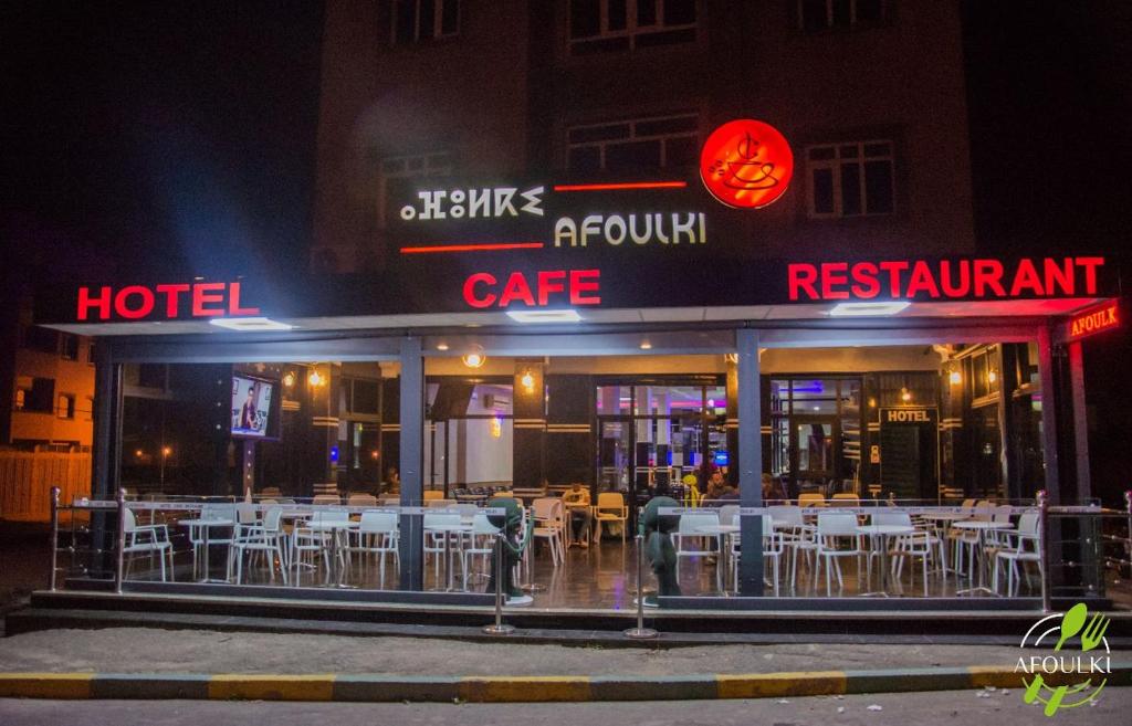 a restaurant with white tables and chairs outside at night at Hôtel Afoulki Tiznit in Tiznit