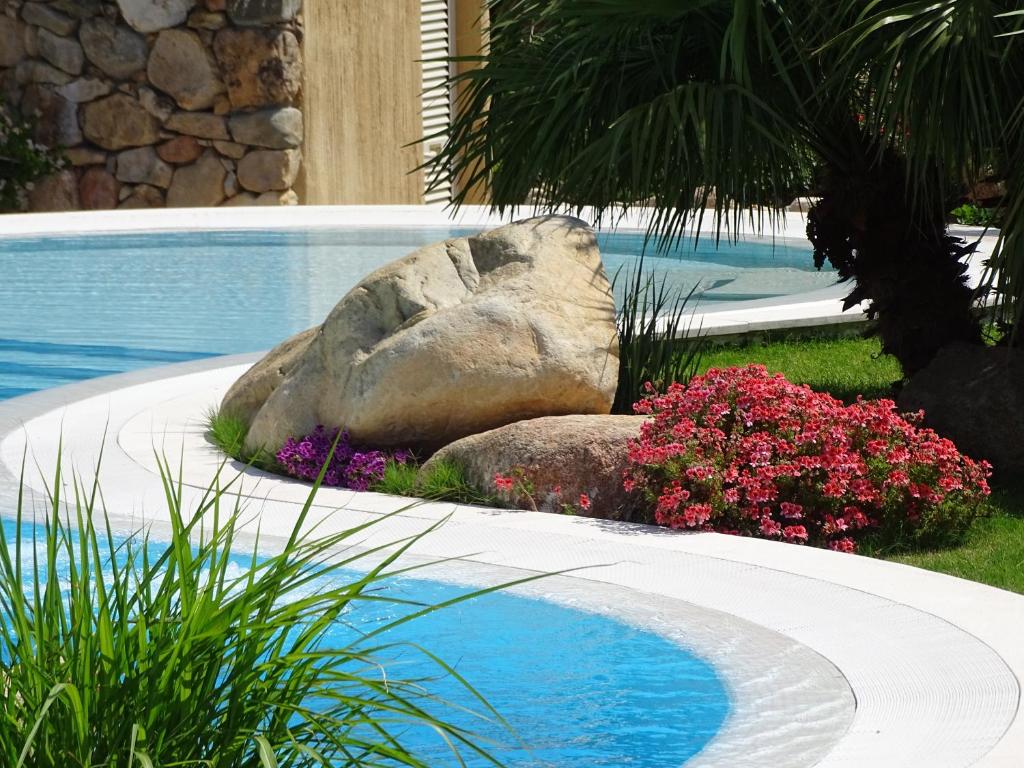 a swimming pool with a rock and flowers in a yard at Hotel Mariposas in Villasimius