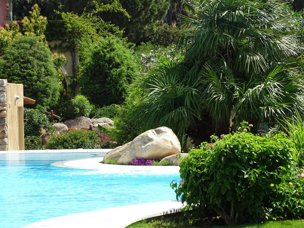 a swimming pool in a garden with a rock and trees at Hotel Mariposas in Villasimius