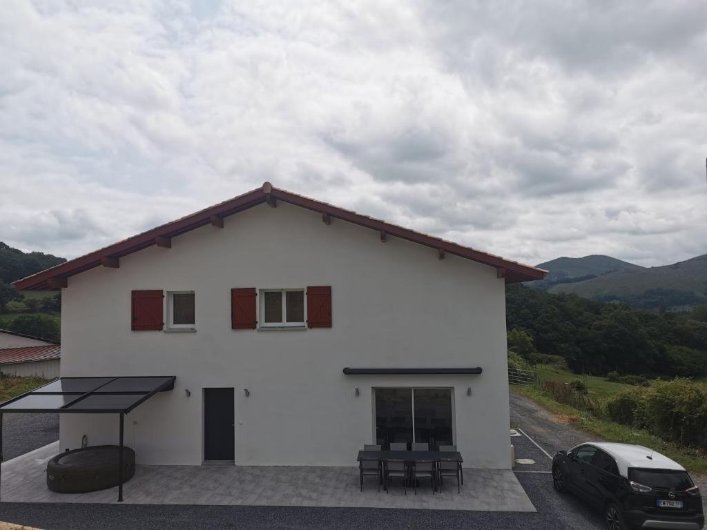a white house with a car parked in front of it at Maison mitoyenne au cœur du Pays Basque in Saint-Esteben
