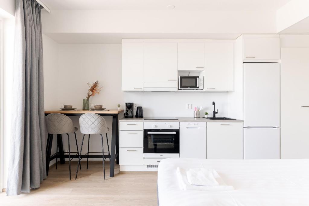 a white kitchen with white cabinets and bar stools at Serviced Apartments Pirkkala by UHANDA in Tampere