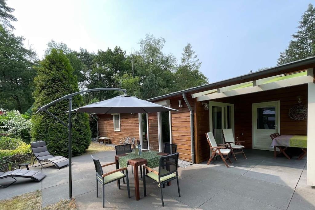 een patio met een tafel en stoelen en een parasol bij Ruime en comfortabele bungalow aan bosrand in Lage Mierde