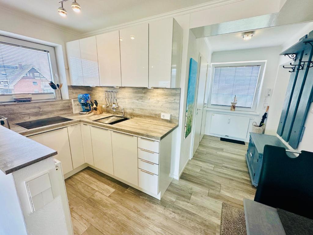 a kitchen with white cabinets and wooden floors and windows at Eidum 209 -strandnah- in Westerland (Sylt)