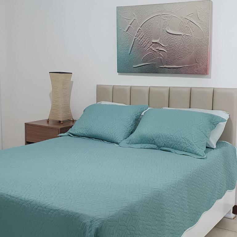 un lit avec des draps bleus et une peinture sur le mur dans l'établissement Confortável apartamento a 100 m Beira Mar - Edifício Zen Residence, à Fortaleza