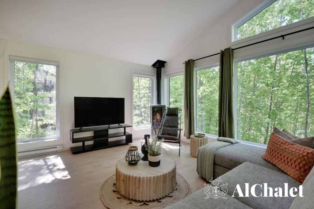 ein Wohnzimmer mit einem Sofa, einem TV und Fenstern in der Unterkunft Arianna- Chalet avec spa & piscine in Pont-Rouge