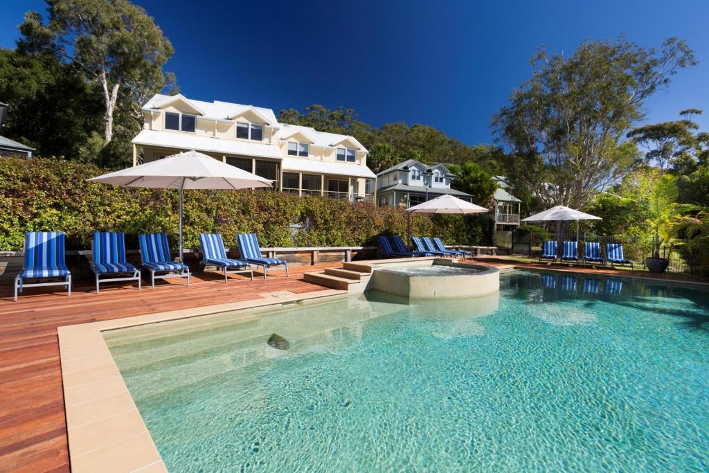 a swimming pool with chairs and umbrellas in front of a house at Blueys Retreat in Blueys Beach