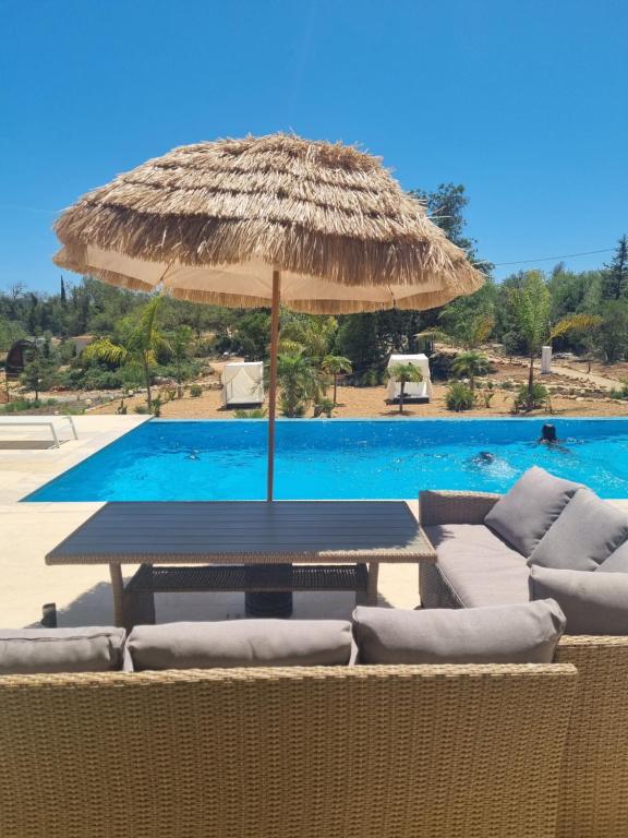 a table with a straw umbrella next to a swimming pool at Eco Lodge Villa das Alfarrobas com Piscina in Algoz