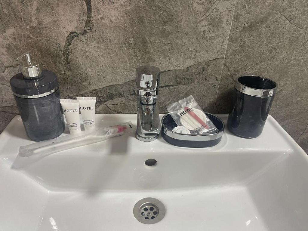 a white sink with toothbrushes and cups on it at Hotel LION Almaty in Almaty