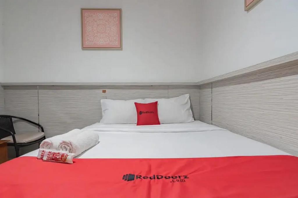 a large white bed with a red pillow on it at RedDoorz At Arwiga Hotel in Bandung