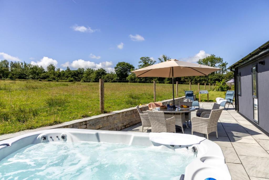 a hot tub on a patio with a table and an umbrella at Cherry Lodge, 14 Roadford Lake Lodges in Lifton