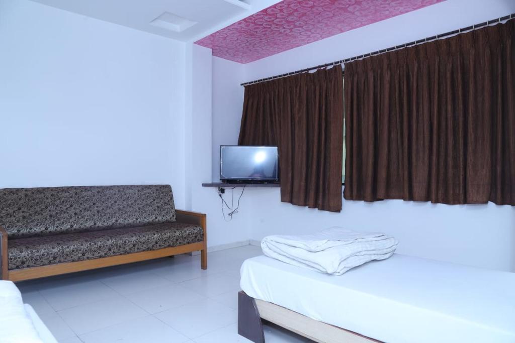 ein Schlafzimmer mit einem Bett, einem Sofa und einem TV in der Unterkunft Hotel Kewal INN in Jālgaon