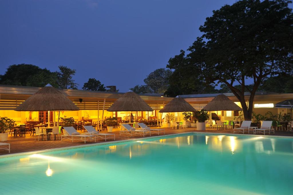 una piscina con sillas, mesas y sombrillas en Cresta Sprayview Victoria Falls en Victoria Falls