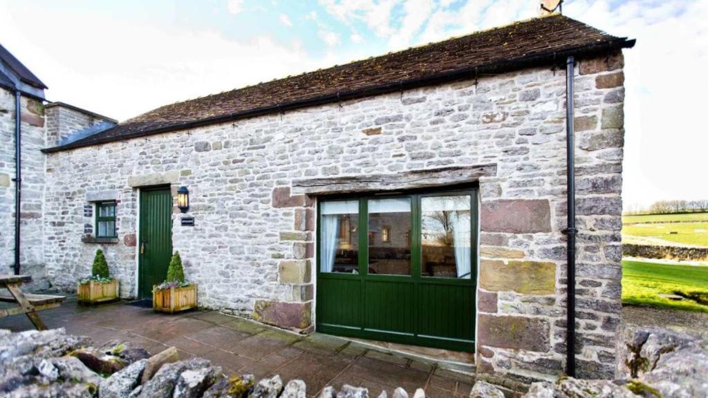 a stone cottage with a green door and a patio at Applegarth in Buxton